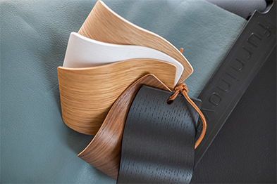 Fanned wood veneer and material swatches with a leather strap on a soft blue surface
