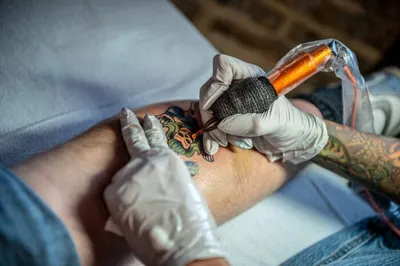 Gloved tattoo artist inking a colorful design on a person's forearm