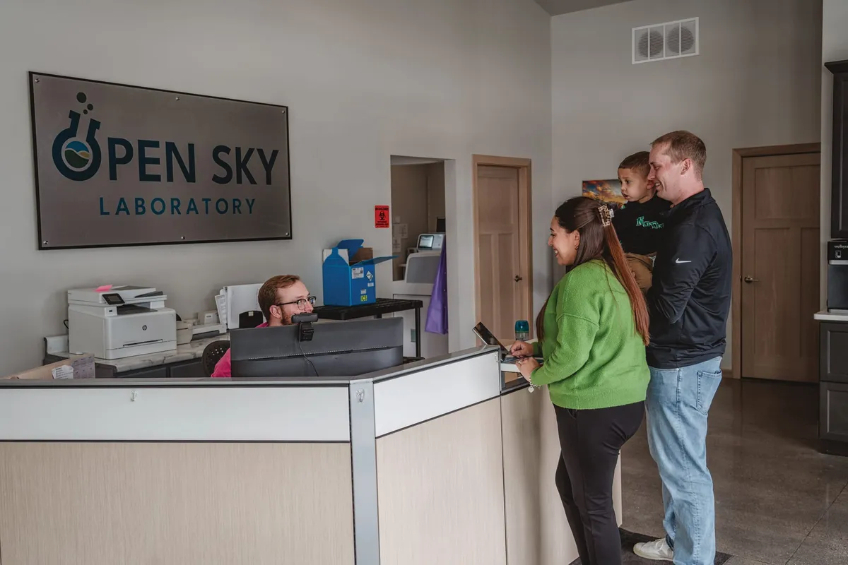 Family of three at the Open Sky Laboratory reception desk speaking with a staff member