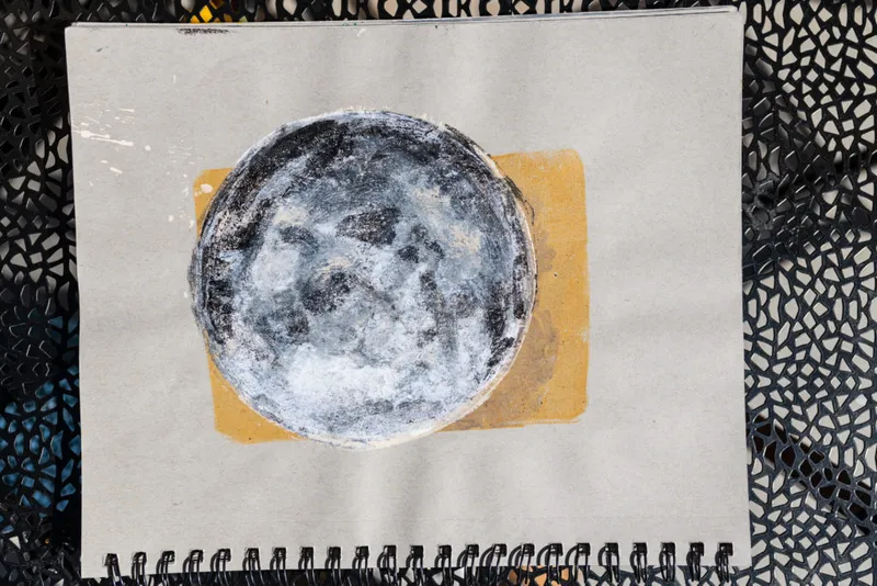 Sketchbook open to a painted full moon with black and white tones over a mustard rectangle