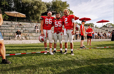 Three American football players in red jerseys numbered 66, 55, and 2 posing on a grass field