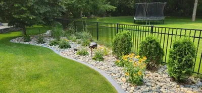 Curved rock garden border with shrubs and yellow flowers along a black metal fence