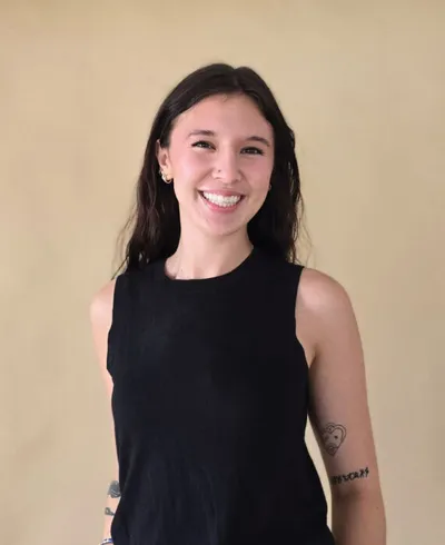 Smiling young woman with dark hair in a black sleeveless top, forearm tattoos visible