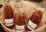Three bottles of red sauce nestled in a straw-lined wooden crate