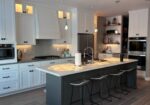 Renovated kitchen with white cabinetry, gray island, bar stools, and open shelving