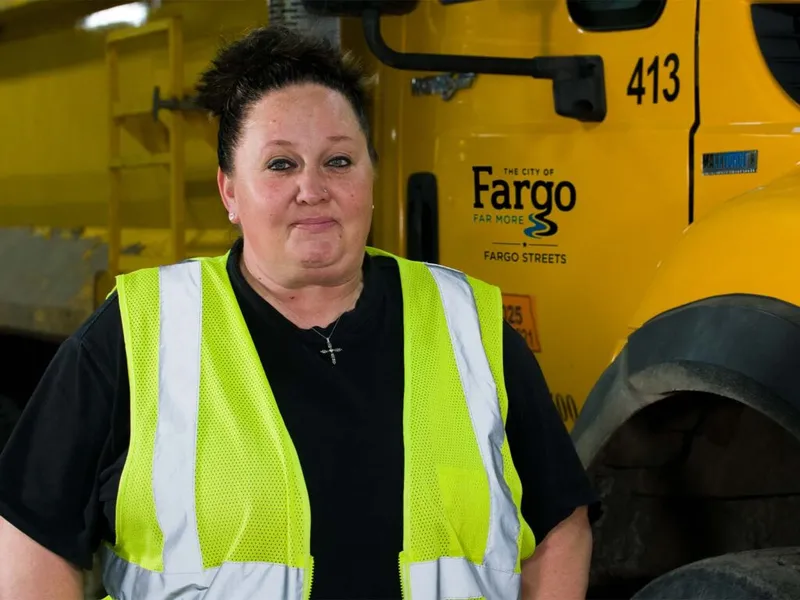 Woman in hi-vis safety vest stands before a yellow City of Fargo Streets truck