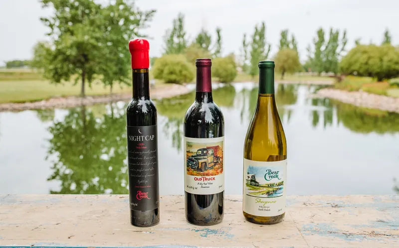 Three Bear Creek Winery bottles—Night Cap, Old Truck, and Shaynne—on a ledge overlooking a pond