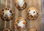 Six chocolate chip cookies with toasted marshmallow centers on parchment paper