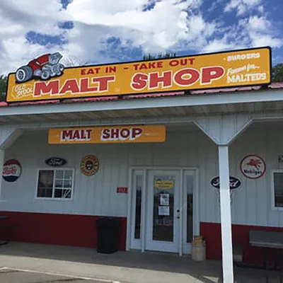 Retro malt shop with yellow signage, vintage brand decals, and a covered entrance