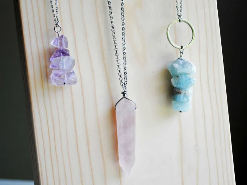 Three crystal pendant necklaces on silver chains displayed against a light wood board