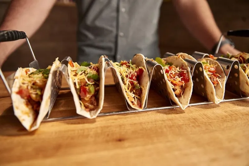 Row of loaded soft tacos in a metal rack on a wooden surface