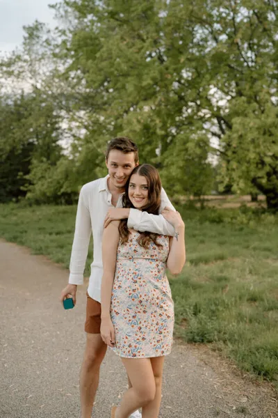 Young couple embracing on a park path, man in white shirt hugging woman in floral dress