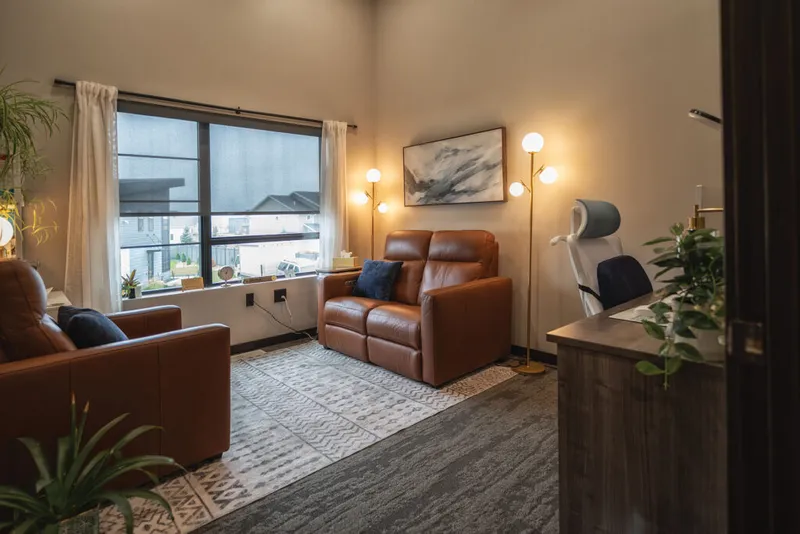 Warmly lit therapy office with two brown leather recliners, floor lamps, and a patterned rug