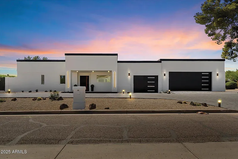 Modern white stucco home with flat roof, two-car garage, and desert landscaping at dusk