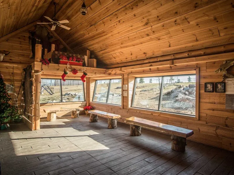 Rustic log cabin interior with log benches, large windows overlooking rocky terrain, and Christmas stockings hanging from a