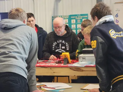 Adult instructor and youth campers working on a project at a table indoors