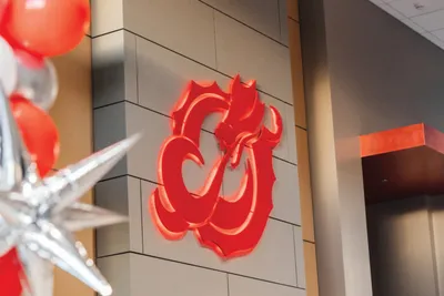 Red dragon logo mounted on a gray tiled wall with red and silver balloons nearby