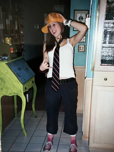 Woman in yellow cap, striped tie, and white tank top posing indoors