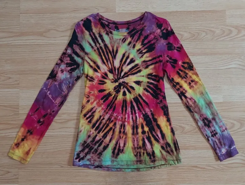 Tie-dye long-sleeve shirt with rainbow swirl pattern on wood surface