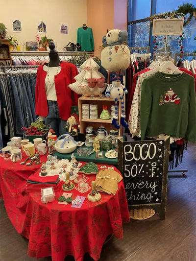 Holiday shop display with red tablecloth, Christmas decor, clothing racks, and a BOGO 50% off chalkboard sign