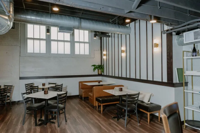 Restaurant dining room with leather booths, ladder-back chairs, and exposed ductwork ceiling