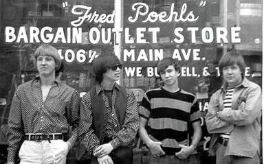Four young men in 1960s attire standing before Fred Poehls Bargain Outlet Store on Main Ave
