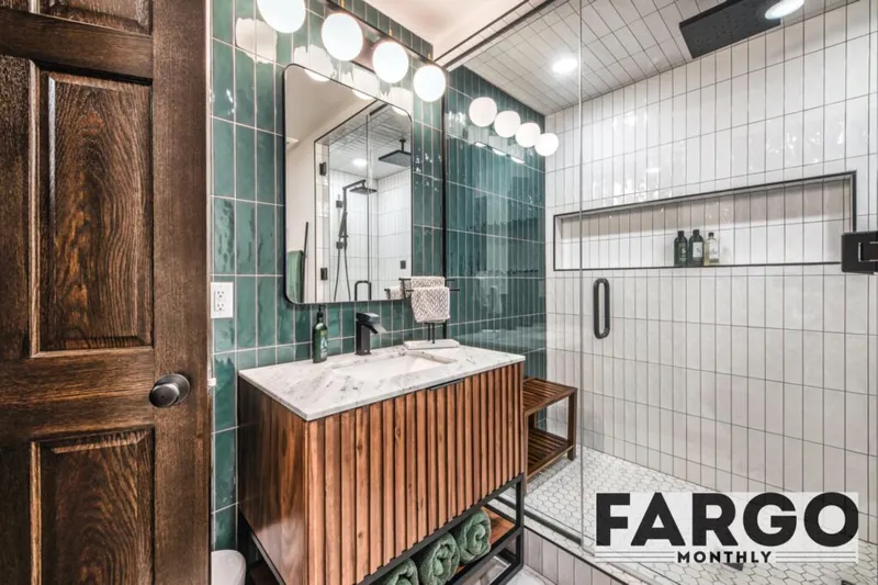Modern bathroom with teal tile accent wall, wood vanity with marble top, and glass-enclosed shower