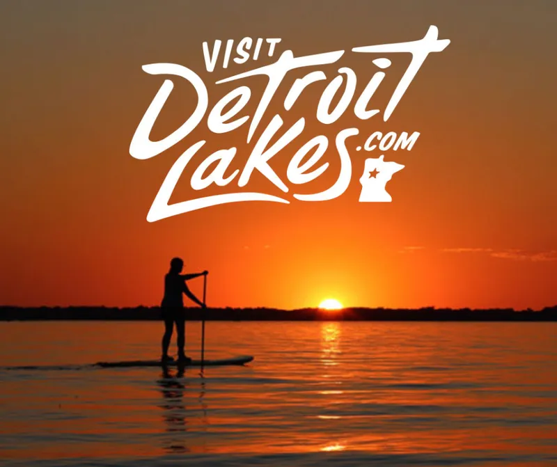 Visit Detroit Lakes logo on sunset over a lake with paddleboarder silhouette