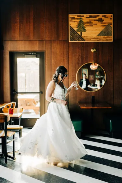 Bride in a flowing white gown holding a champagne flute in a wood-paneled restaurant