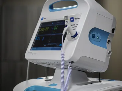 White and blue medical vital signs monitor with attached probe on a stand