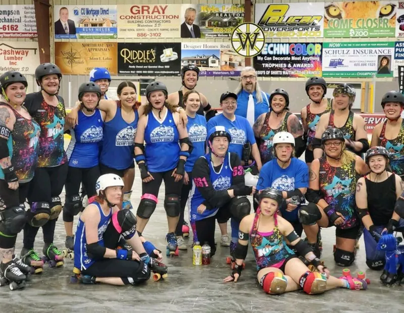 Two roller derby teams posing together on a rink in helmets and pads