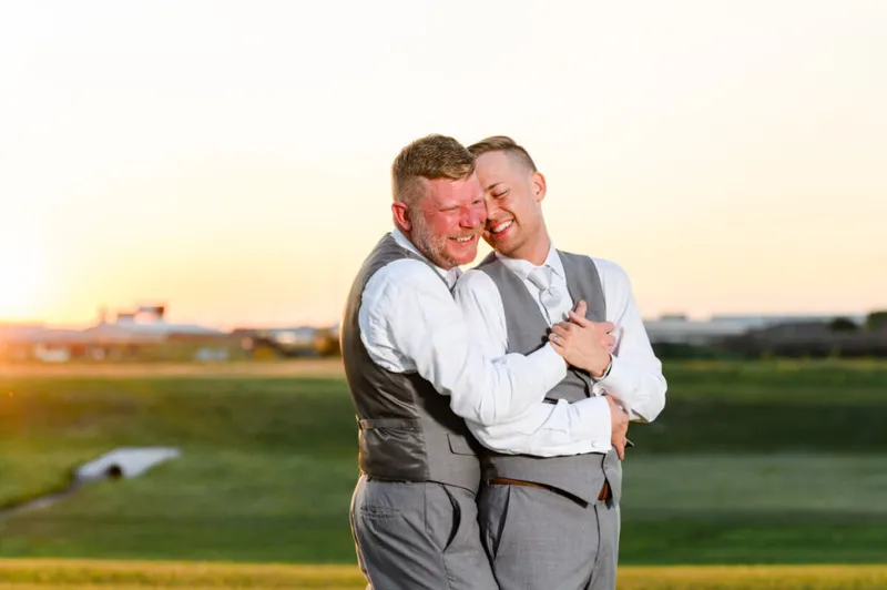 Two men in gray suits embracing and laughing at golden hour on a green field