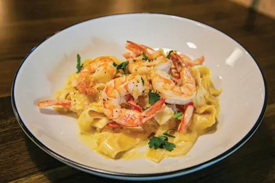 Creamy fettuccine pasta topped with sautéed shrimp and fresh herbs on a white plate