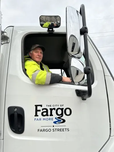 A worker in a hi-vis jacket looks out from a City of Fargo Streets truck cab