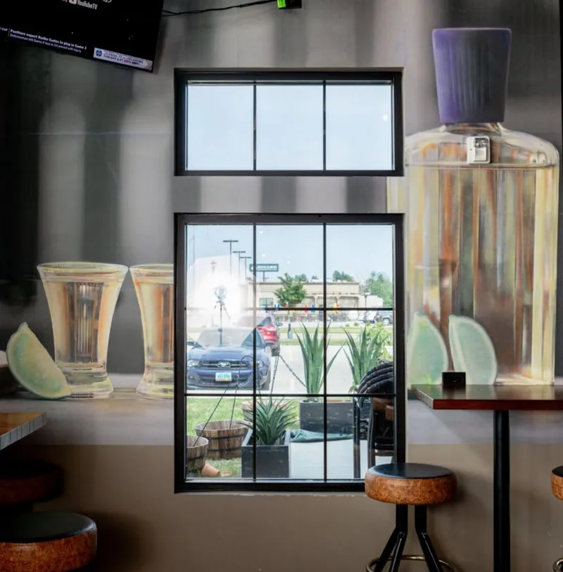 Bar interior mural of oversized tequila bottle and shot glasses with lime beside a street-view window