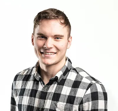 Smiling young man with short hair and nose ring in a black-and-white plaid shirt