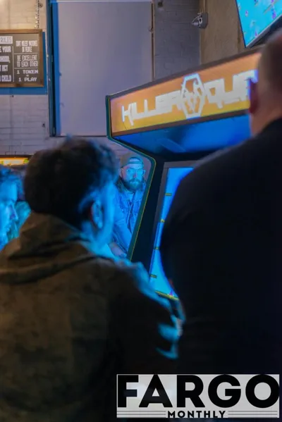 Two people playing a Killer Instinct arcade cabinet bathed in blue light
