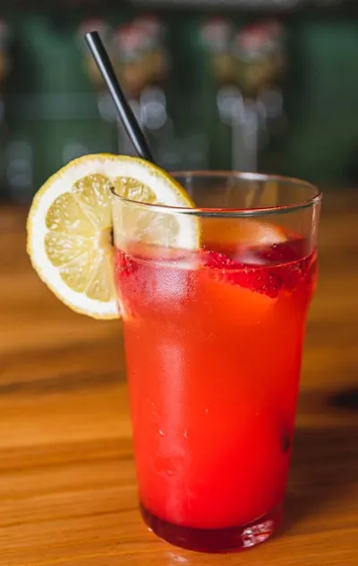 Red iced drink with a lemon slice garnish and black straw on a wooden bar