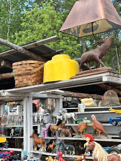 Outdoor flea market shelves crowded with toy animals, a deer lamp, wicker basket, and yellow container