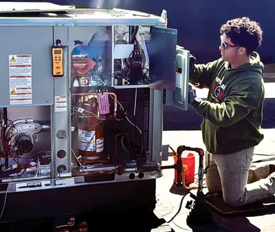 Technician kneeling beside an open rooftop HVAC unit inspecting internal components