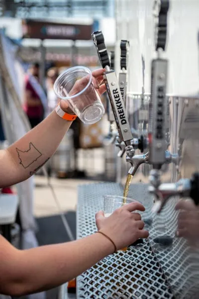 Tattooed arm pouring beer from a Drekker tap handle at an outdoor festival