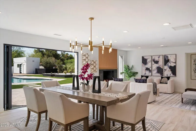 Open-plan dining and living room with gold chandelier, fireplace, and folding doors opening to a backyard pool