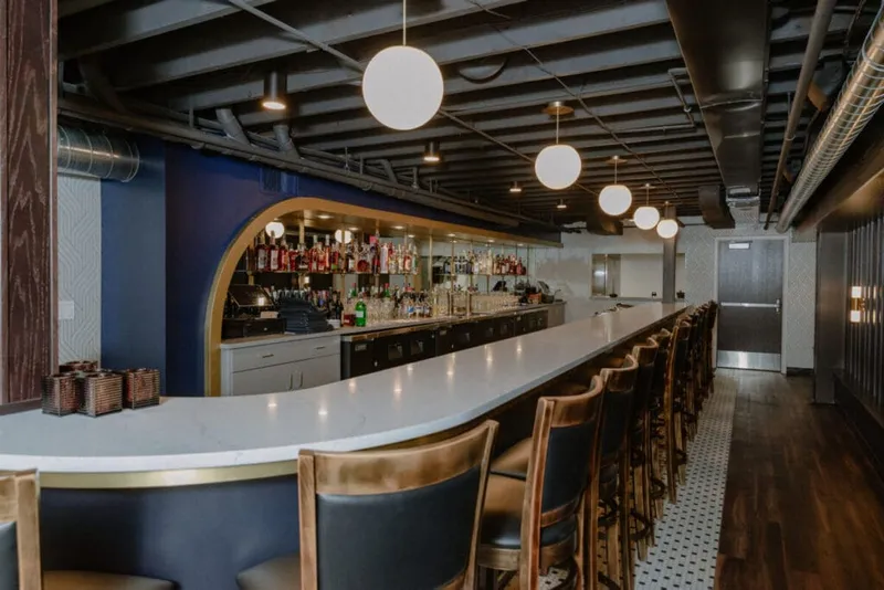 Curved white marble bar with leather stools beneath globe pendant lights in a moody blue-accented cocktail lounge