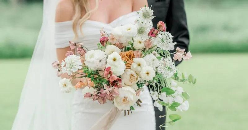 Bride in off-shoulder white gown holding a lush bouquet of white, pink, and peach blooms
