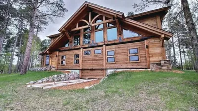 Large log cabin lodge surrounded by tall pine trees on a grassy hillside
