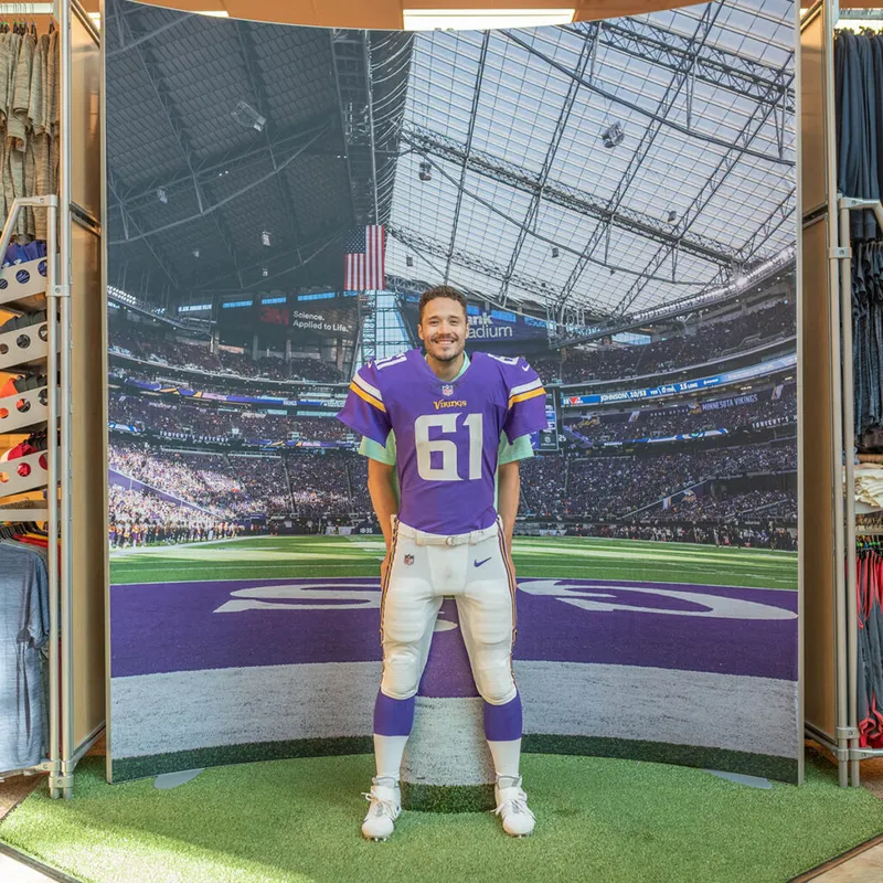 Man in Vikings jersey number 61 stands in a stadium photo-op display inside a retail store