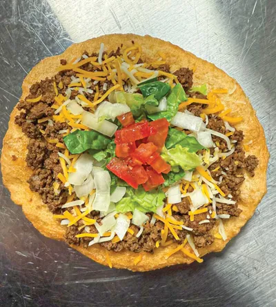 Tostada topped with seasoned ground beef, shredded cheese, lettuce, tomato, and onion