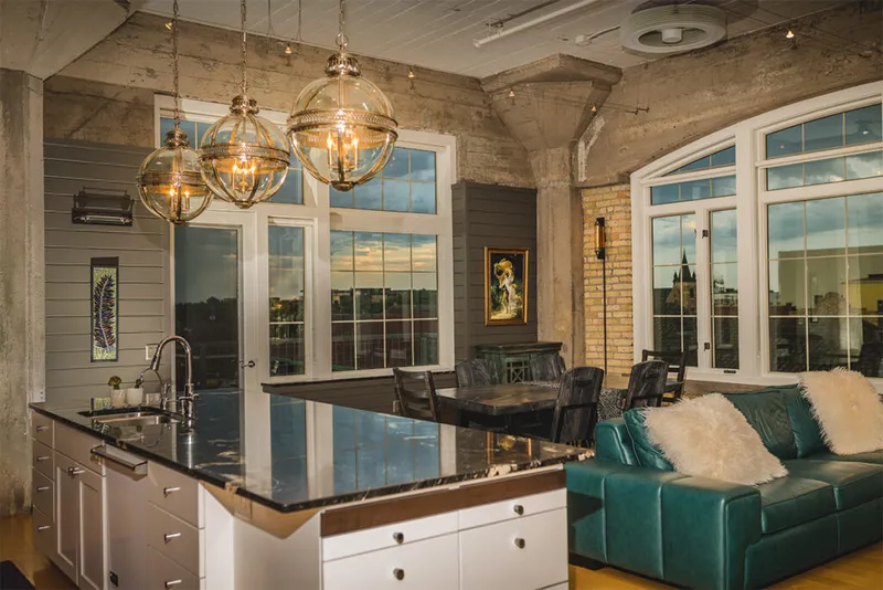 Open-concept loft interior with dark granite island, globe pendant lights, and teal leather sofa