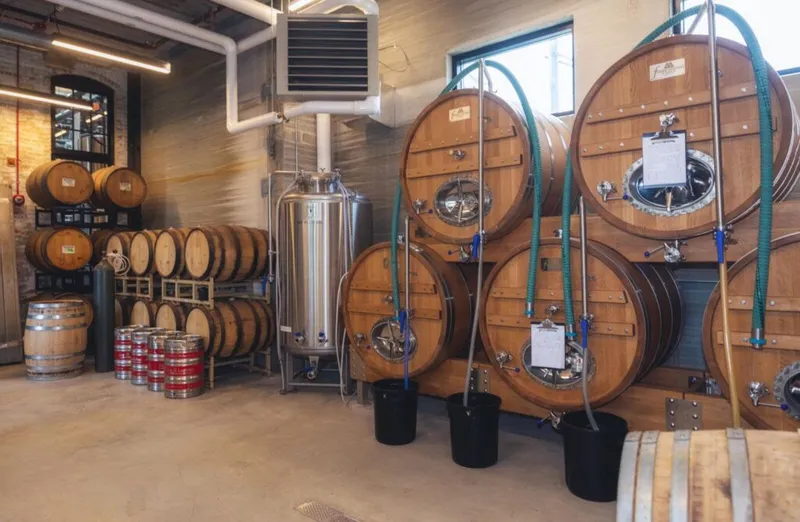 Large wooden fermentation tanks and oak barrels inside a brewery production facility