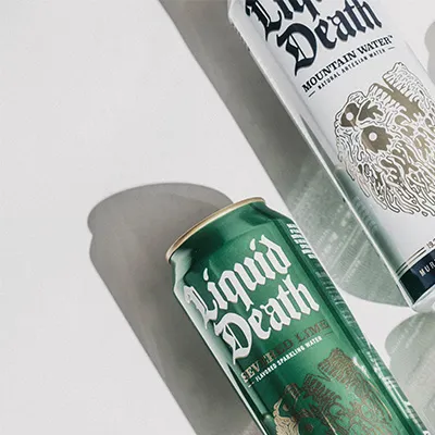 Green and white Liquid Death sparkling and still water cans on a light surface